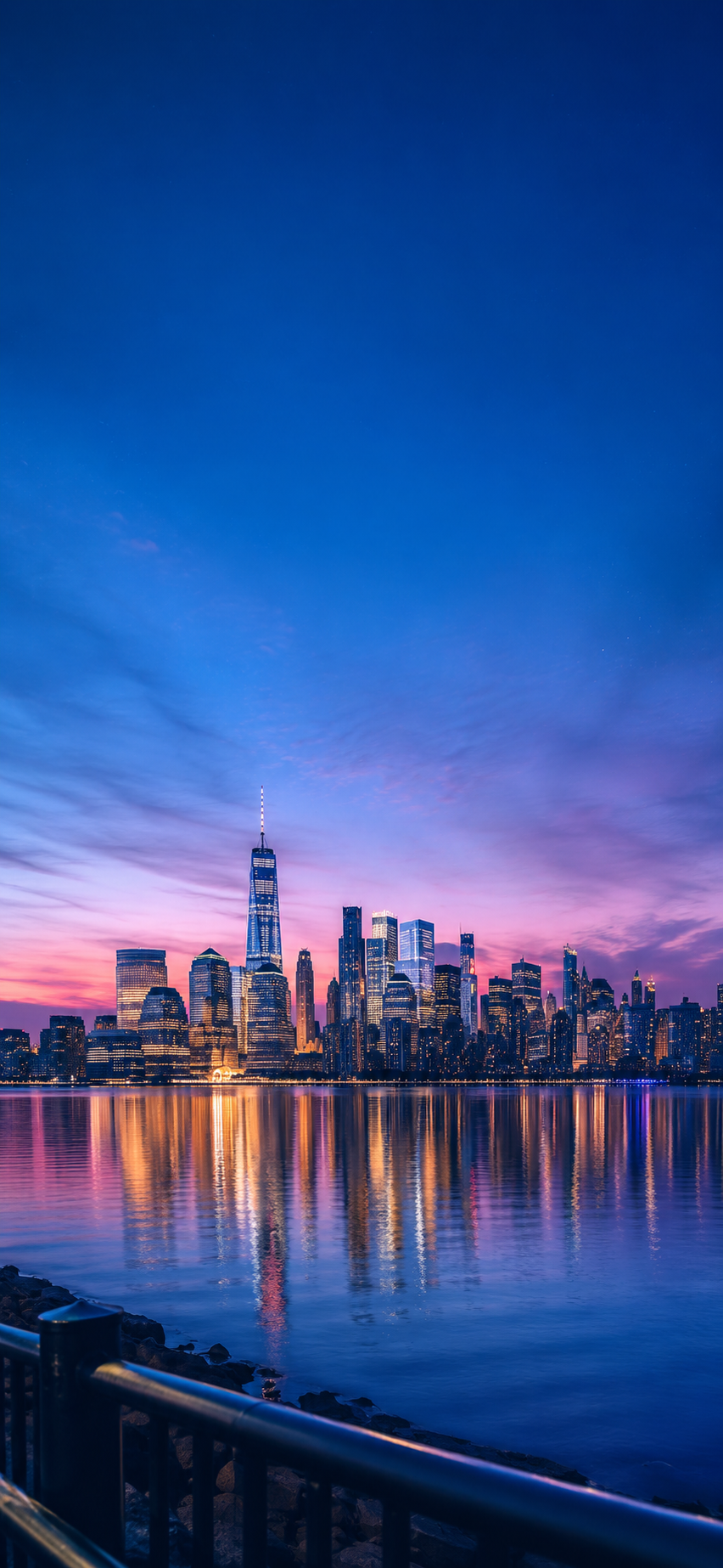Manhattan blue hour phone wallpaper with skyline reflections and soft pink clouds over the river.