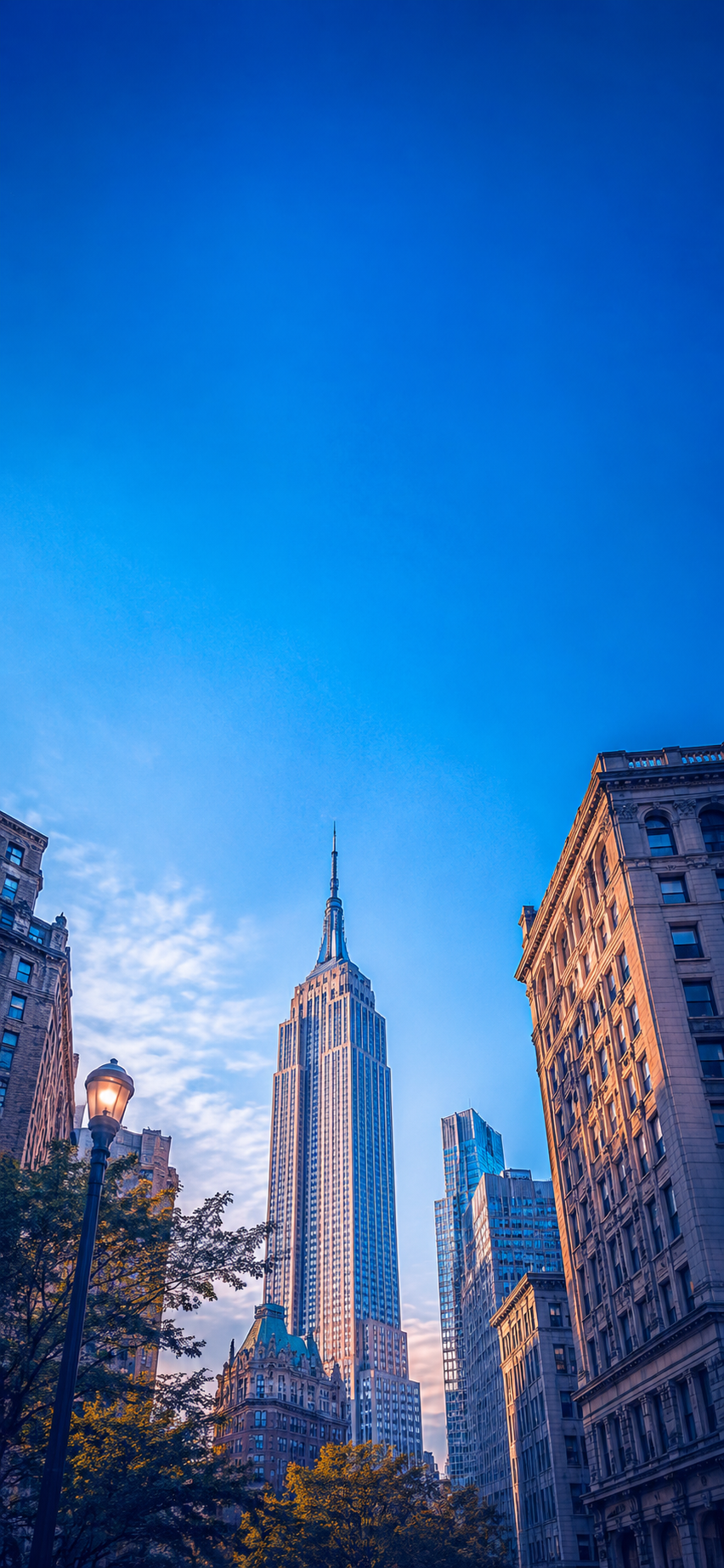 Empire State Building phone wallpaper from a New York avenue with blue sky and city buildings.