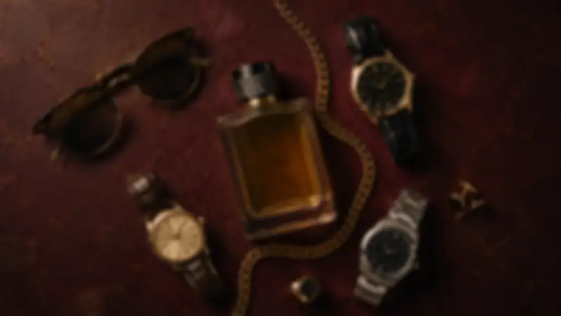 Round sunglasses, amber fragrance bottle, three watches, cufflinks, and chain on burgundy plaster.