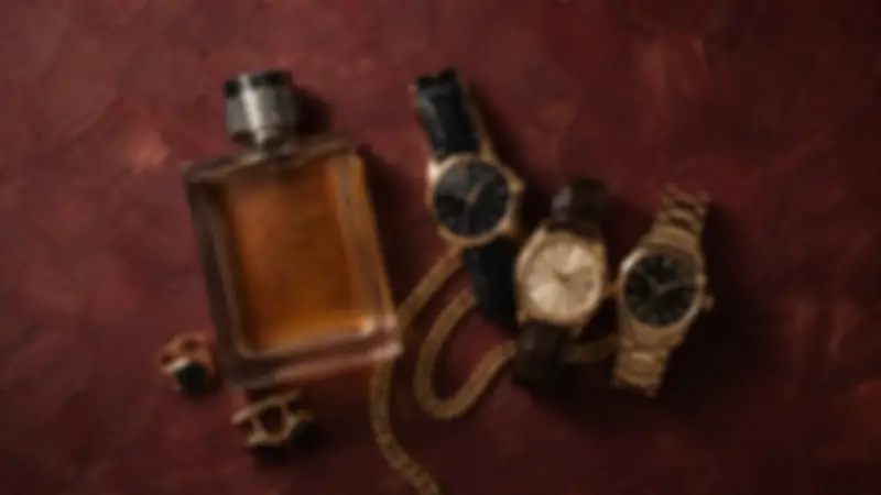 Three watches, amber fragrance, gold chain, ring, and cufflinks on burgundy textured plaster.