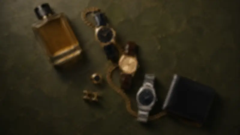 Black wallet, amber fragrance, three watches, ring, cufflinks, and chain on forest-green plaster.