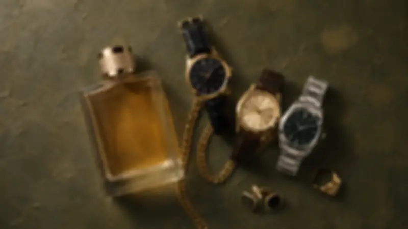 Amber fragrance, three watches, cufflinks, a ring, and gold chain on deep olive textured plaster.
